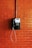 A vintage public telephone mounted on a brick wall. The phone is black with a coiled cord and a numeric keypad. A pipe runs vertically above the phone.