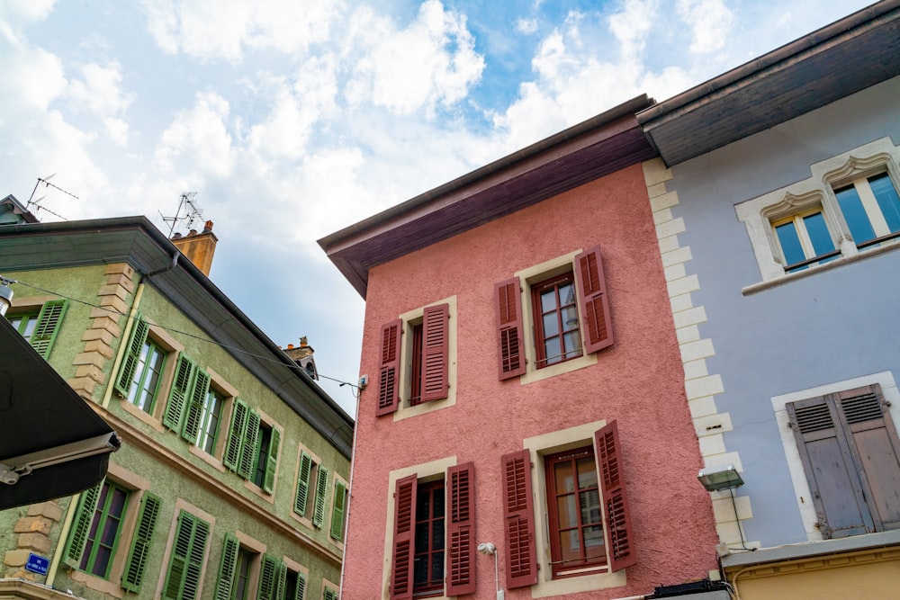 a pink building with green shutters next to other buildings