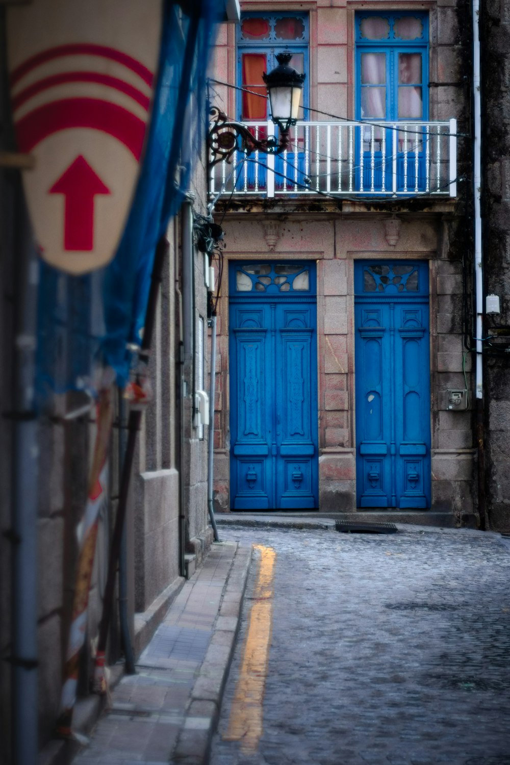 a narrow alleyway with blue doors and a balcony