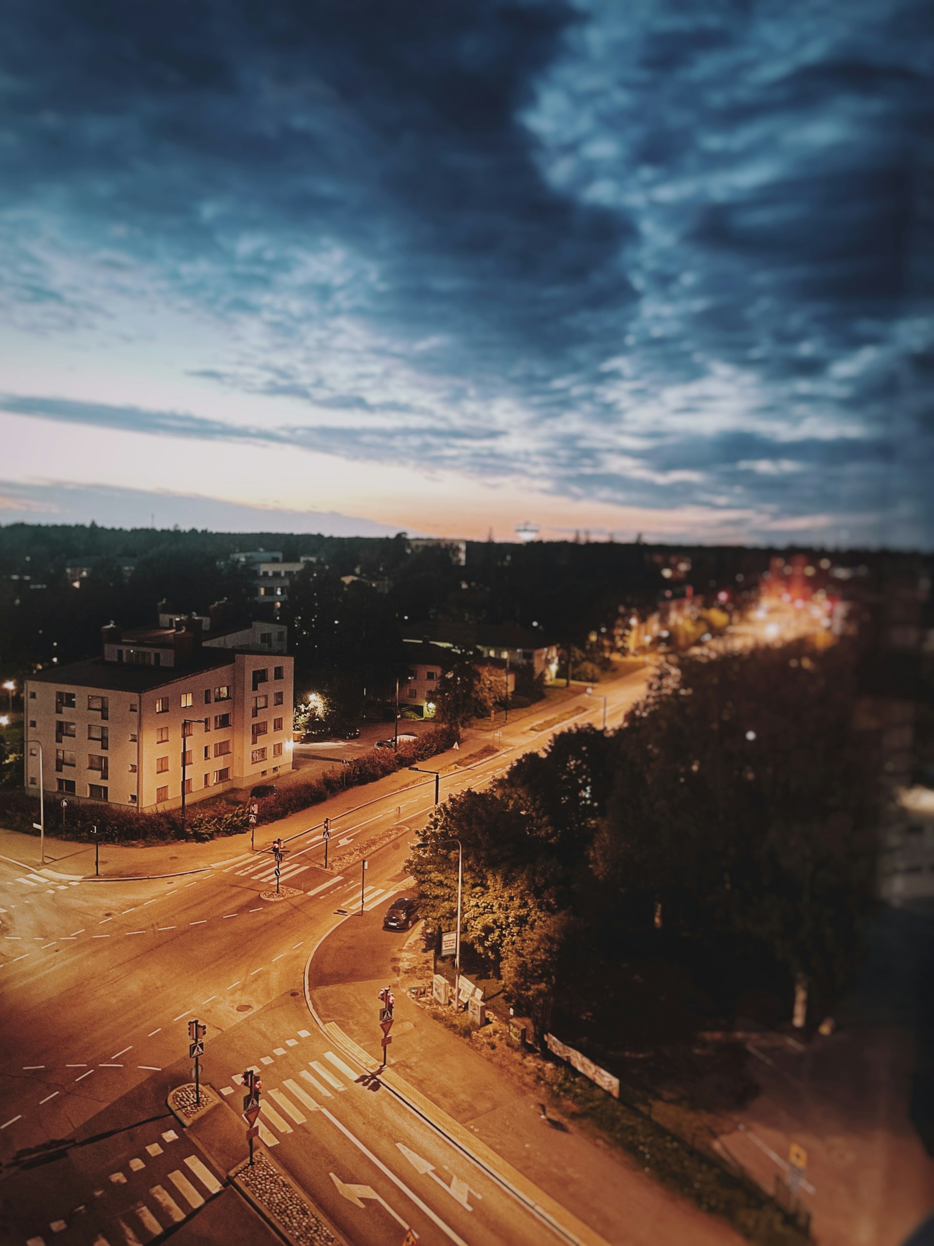 A serene cityscape at dusk, with glowing streetlights casting warm reflections on wet asphalt.
