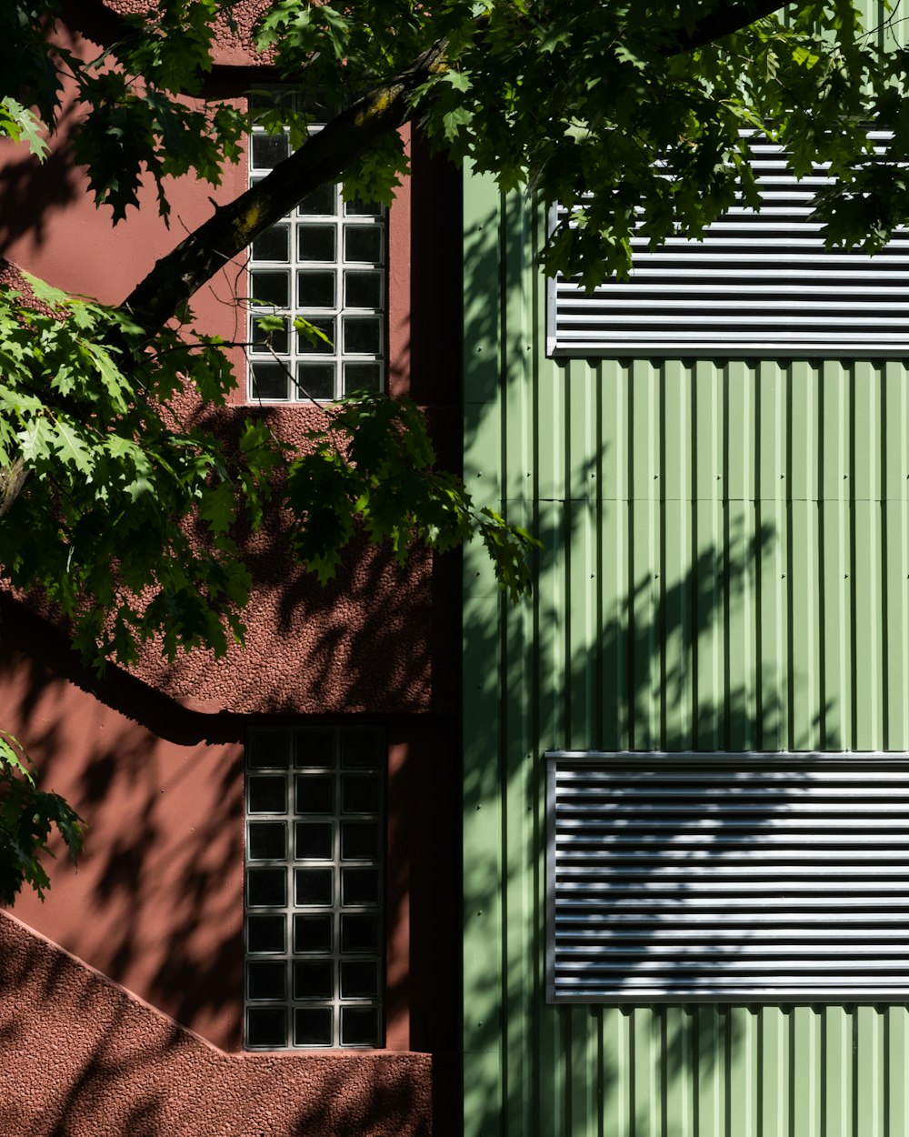 a green building with two windows and a tree in front of it