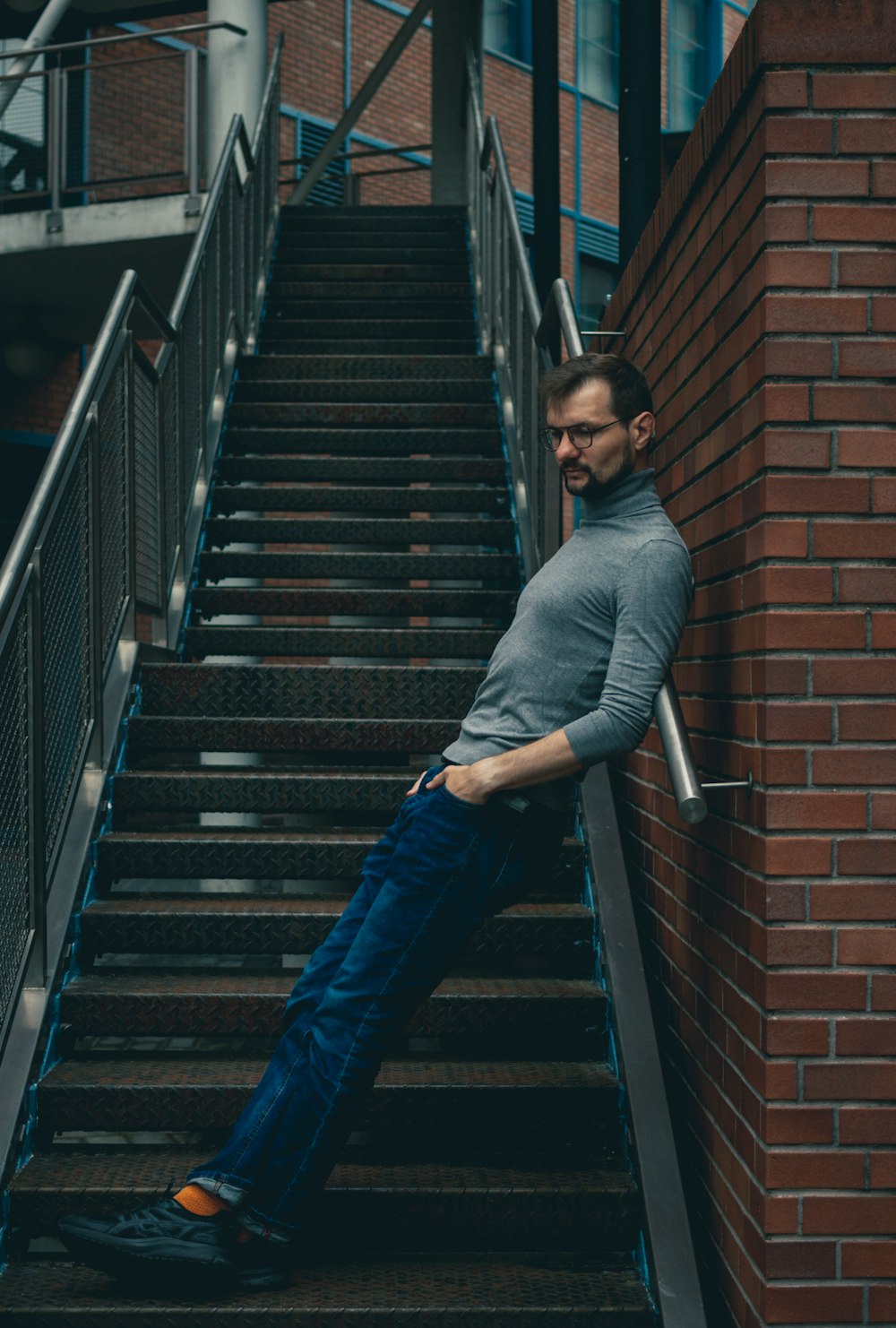a man leaning against a brick wall next to a set of stairs