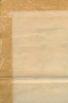An aged, textured sheet of paper with visible folds and a bordered pattern. The paper has a yellowish-brown tint, indicating it is old or possibly stained.