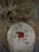 An embroidery hoop displays a detailed image of a curled-up fox surrounded by leaves. The background features a woven mat and a small pair of golden embroidery scissors. A bundle of dried wheat stalks is placed nearby, adding a natural, rustic feel.