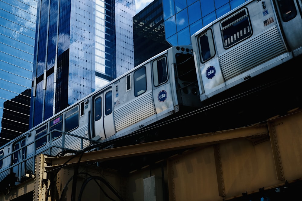 a silver train traveling over a bridge next to tall buildings