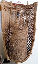 A traditional woven basket with intricate and natural textures. Inside the basket, there is a bundle of dried, tangled fibers or straw.