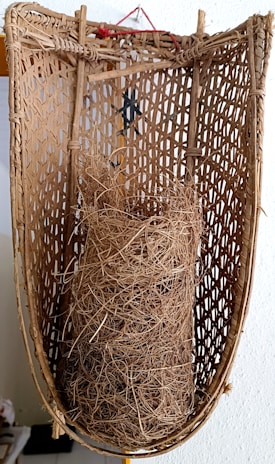 A traditional woven basket with intricate and natural textures. Inside the basket, there is a bundle of dried, tangled fibers or straw.