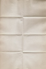 An aged, beige paper with visible creases running vertically and horizontally, giving it a worn and folded appearance. The texture is slightly rough and the color is uniform throughout.
