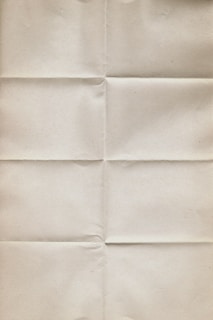 An aged, beige paper with visible creases running vertically and horizontally, giving it a worn and folded appearance. The texture is slightly rough and the color is uniform throughout.