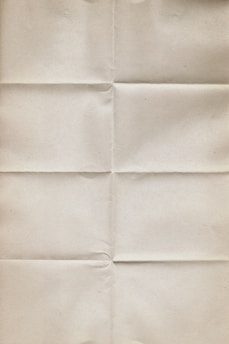 An aged, beige paper with visible creases running vertically and horizontally, giving it a worn and folded appearance. The texture is slightly rough and the color is uniform throughout.