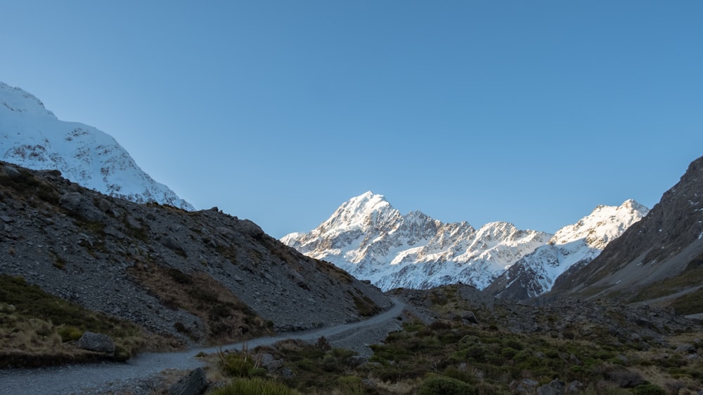 a dirt road in the mountains with snow capped mountains in the background