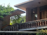 A modern architectural structure with brick walls surrounded by lush greenery. The design features flat overhanging roofs and large wooden windows, creating a harmonious blend of nature and contemporary design.