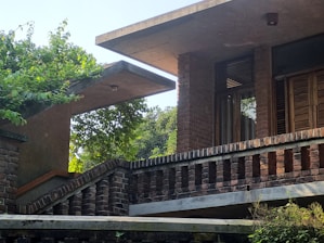 A modern architectural structure with brick walls surrounded by lush greenery. The design features flat overhanging roofs and large wooden windows, creating a harmonious blend of nature and contemporary design.