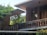 A modern architectural structure with brick walls surrounded by lush greenery. The design features flat overhanging roofs and large wooden windows, creating a harmonious blend of nature and contemporary design.