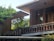 A modern architectural structure with brick walls surrounded by lush greenery. The design features flat overhanging roofs and large wooden windows, creating a harmonious blend of nature and contemporary design.