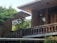 A modern architectural structure with brick walls surrounded by lush greenery. The design features flat overhanging roofs and large wooden windows, creating a harmonious blend of nature and contemporary design.