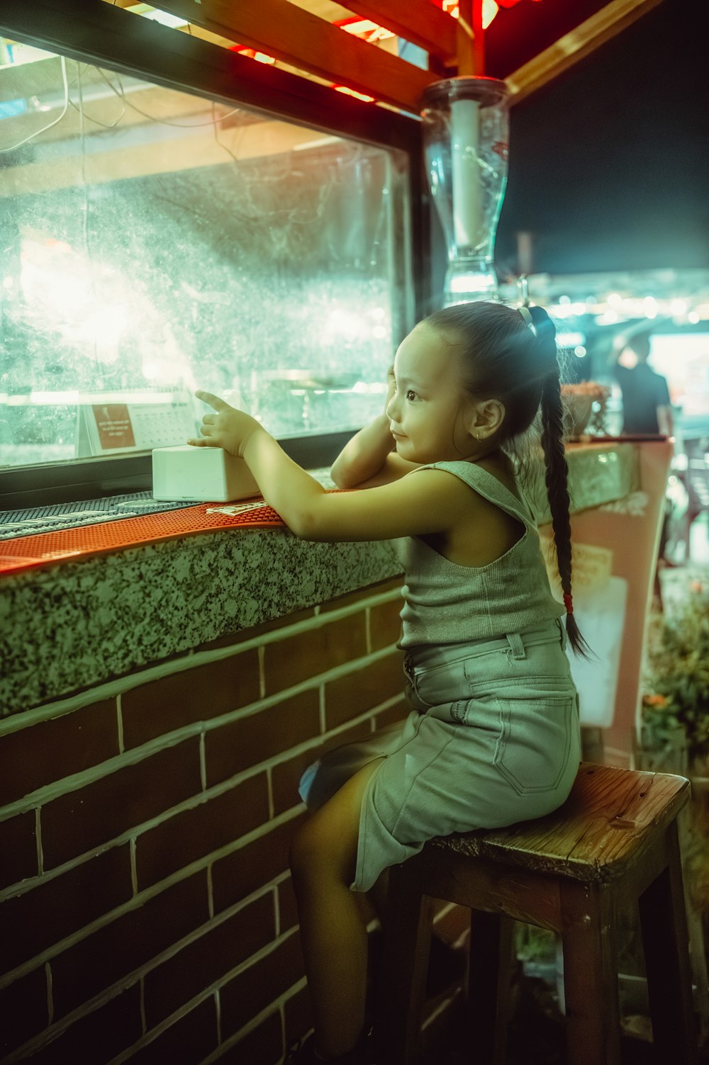 a little girl sitting on a stool looking out a window