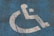A weathered and cracked wheelchair accessibility symbol painted in white on a blue surface.