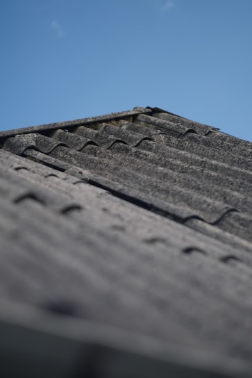 A close-up of a freshly installed roof shrink wrap tightly covering a residential roof under a clear blue sky.