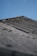 A close-up view of a grey corrugated roof under a clear blue sky. The surface of the roof shows signs of wear and age, with slight discoloration and moss growth along the edges.