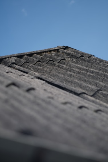 A close-up of a StormGuard Roofing crew carefully inspecting a shingled roof under a bright blue sky.