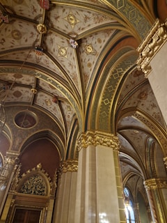 Ornate, vaulted ceilings with elaborate patterns and detailed gilded decorations are visible. The architectural design includes rich gold embellishments and intricate artwork on a textured background.