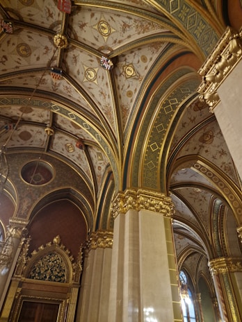 Ornate, vaulted ceilings with elaborate patterns and detailed gilded decorations are visible. The architectural design includes rich gold embellishments and intricate artwork on a textured background.