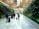 A group of people with suitcases walk through a spacious corridor lined with lush vertical gardens on both sides. The ceiling features hanging greenery and wooden lattice structures, creating an inviting and modern atmosphere.