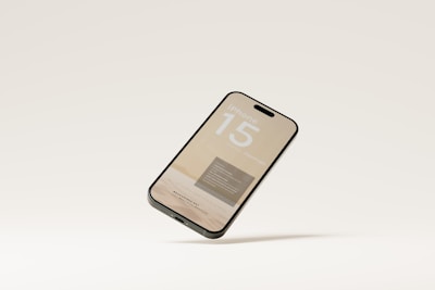 A smartphone is depicted floating against a plain, light-colored background. The screen displays text and graphics, suggesting a promotional or mock-up design for an iPhone 15.