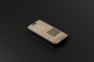 A smartphone with a sleek design is lying on a dark surface. The screen displays information with the text 'iPhone 15' prominently featured, along with some unreadable smaller text.