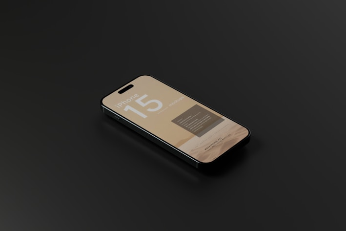 A smartphone with a sleek design is lying on a dark surface. The screen displays information with the text 'iPhone 15' prominently featured, along with some unreadable smaller text.