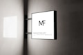 A modern square sign with the letters 'MF' is mounted on a wall. The sign has a minimalistic design with a black frame and a white background. The text 'MOCKUPFREE.NET' and 'REALISTIC MOCKUPS' is written at the bottom in smaller font. The background is a smooth, light-colored wall with subtle shadows.