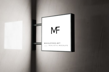 A modern square sign with the letters 'MF' is mounted on a wall. The sign has a minimalistic design with a black frame and a white background. The text 'MOCKUPFREE.NET' and 'REALISTIC MOCKUPS' is written at the bottom in smaller font. The background is a smooth, light-colored wall with subtle shadows.