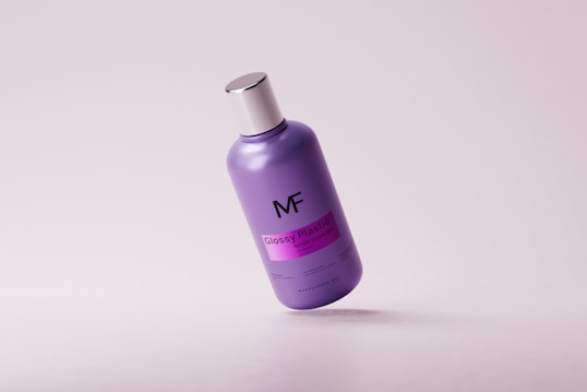 A purple plastic bottle with a metallic silver cap, labeled with 'MF' and 'Glossy Plastic Bottle Mockup.' The bottle is tilted and situated on a clean, light-colored background, casting a subtle shadow beneath.