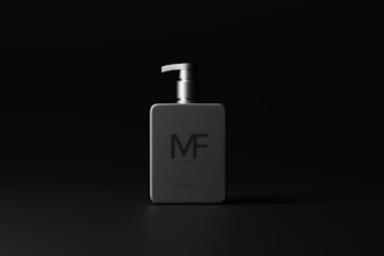 A modern, minimalistic bottle with a dispenser pump is centered on a dark background. The bottle is sleek and square, featuring the letters 'MF' prominently on the front. The design is clean and understated, emphasizing sophistication.