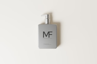 A minimalist silver pump bottle is centered on a light cream background. The bottle features a clean and modern design with simple text and a pump dispenser.