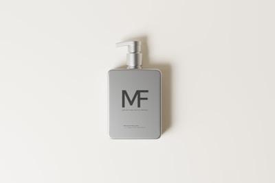 A minimalist silver pump bottle is centered on a light cream background. The bottle features a clean and modern design with simple text and a pump dispenser.
