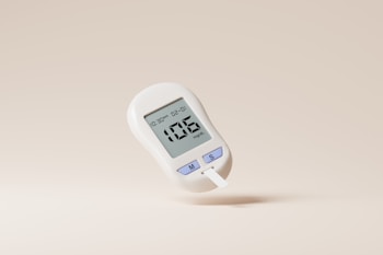A digital glucose meter displaying a reading of 106 mg/dL. The device is predominantly white with purple buttons labeled with 'M' and 'S'. A test strip is inserted into the bottom of the meter. The background is a plain, light beige color.