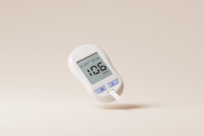 A digital glucose meter displaying a reading of 106 mg/dL. The device is predominantly white with purple buttons labeled with 'M' and 'S'. A test strip is inserted into the bottom of the meter. The background is a plain, light beige color.