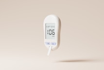 A white digital glucose meter displaying a reading of 106 mg/dL is set against a plain beige background. The device includes buttons labeled 'M' and 'S' and shows a timestamp on its screen.