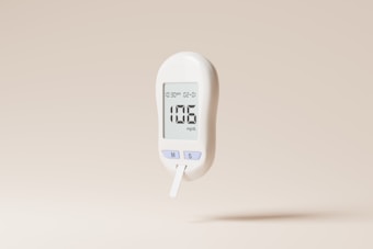 A white digital glucose meter displaying a reading of 106 mg/dL is set against a plain beige background. The device includes buttons labeled 