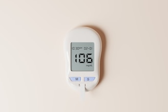 A digital glucose meter displaying a blood sugar reading of 106 mg/dL, with a date and time shown as 10:30 am on 02-01. The device features two buttons labeled 'M' and 'S' and is designed in a sleek, modern style on a plain, light background.