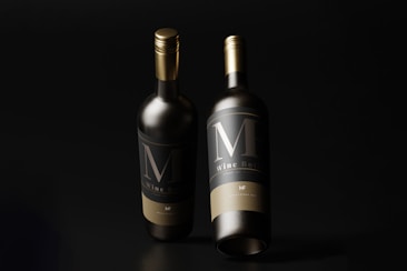 Two elegant wine bottles with dark labels and gold caps stand against a black background. The lighting highlights the bottles, creating a sophisticated and luxurious feel.