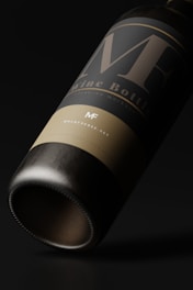 A close-up view of a wine bottle with a minimalist and elegant design. The label features large, stylized letters and subtle text beneath. The bottle is tilted on its side against a dark background, emphasizing the sleek and polished appearance.