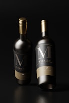Two elegant wine bottles with a sleek design featuring gold caps. The labels prominently display large initials 'MF' in an understated yet sophisticated style, accompanied by smaller text below. The bottles are set against a dark background, emphasizing their dark, glossy appearance.