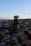 A stack of smooth stones is balanced on a rocky beach, with the ocean and sky in the background. The scene gives an impression of tranquility and balance.