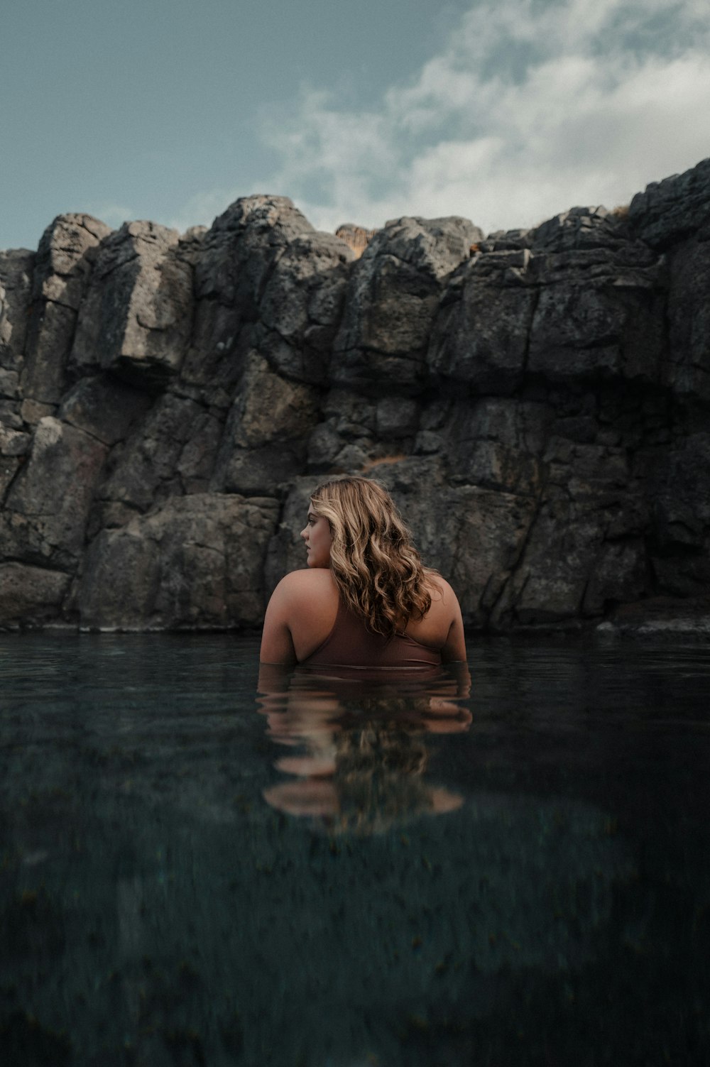 a woman in a body of water with rocks in the background