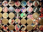 A collection of vintage film reel canisters decorated with colorful images from classic movies. The canisters feature a variety of scenes and actors from different films, showcasing vibrant outfits and dramatic expressions.