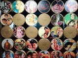 A collection of vintage film reels with covers featuring classic Indian movie posters. The reels are organized in a grid pattern, with colorful and artistic illustrations of actors and scenes from various films. Some reels have labels with titles or quotes.