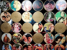 A collection of vintage film reels with covers featuring classic Indian movie posters. The reels are organized in a grid pattern, with colorful and artistic illustrations of actors and scenes from various films. Some reels have labels with titles or quotes.